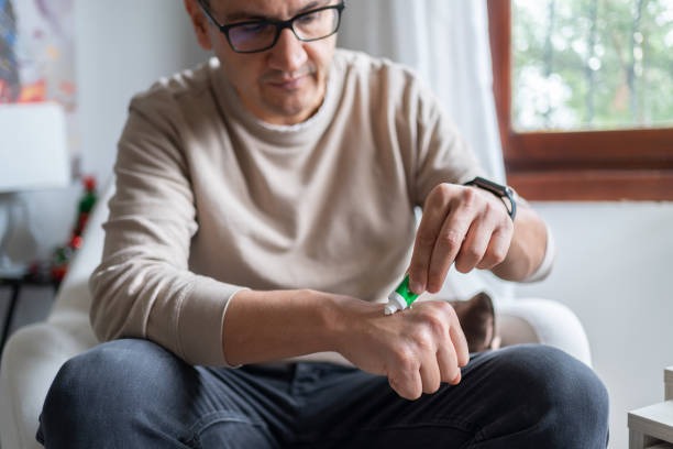 Man seated in a white armchair applying anti-itch cream to a bug bite on his wrist