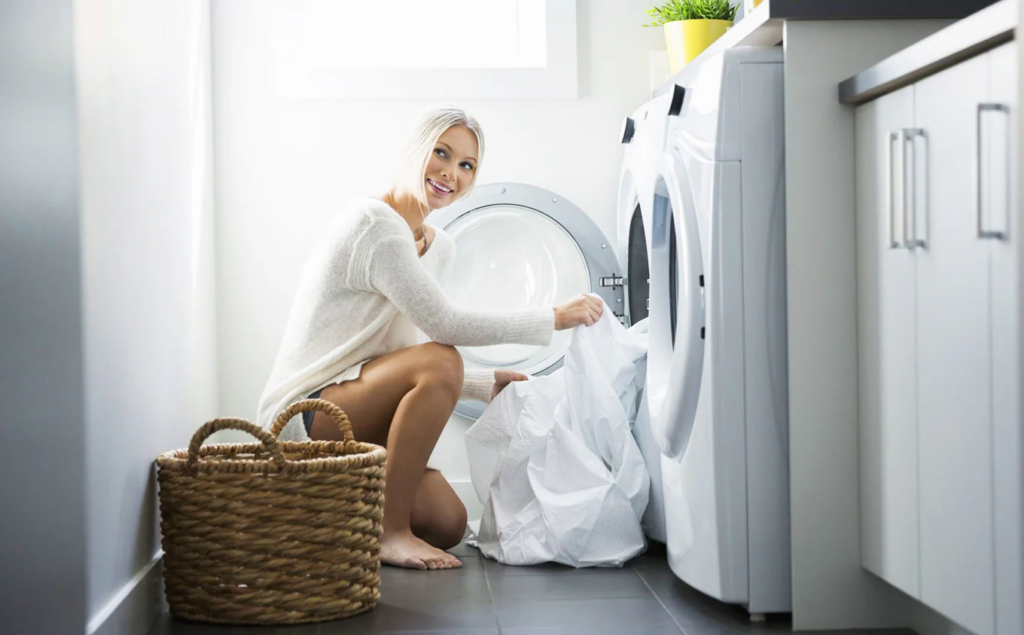 Smiling woman loading white laundry into a front-loading washing machine.