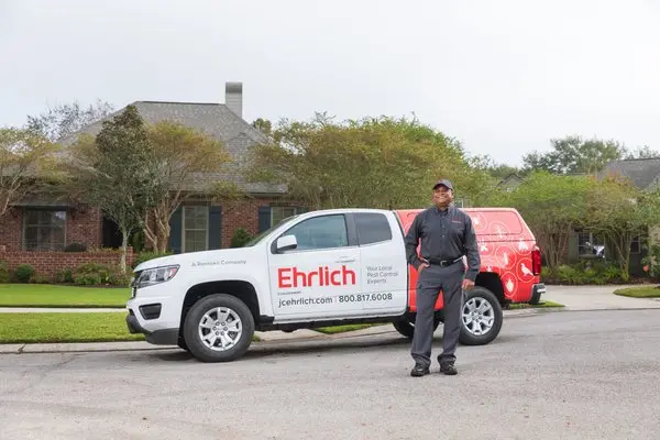 Ehrlich pest control technician standing in front of a branded Ehrlich service truck.