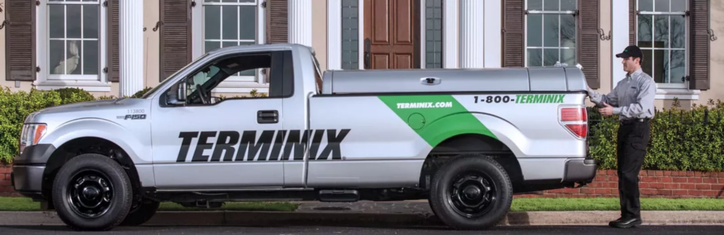 Terminix pest control technician standing next to a branded Terminix service truck outside a home.