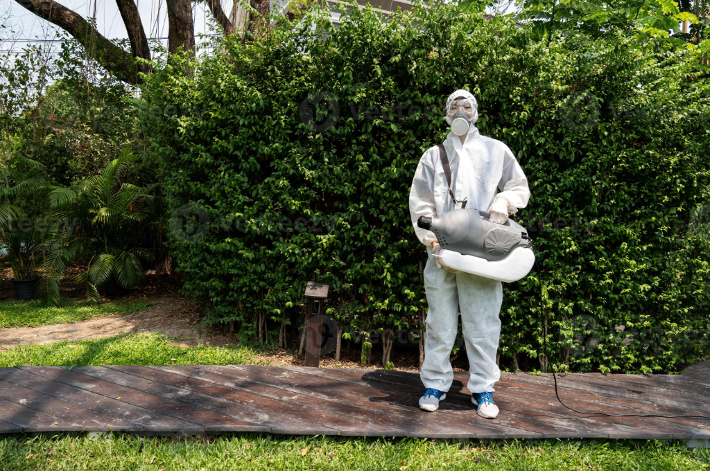Pest control technician in a white hazmat suit and respirator using a fogging machine on a deck