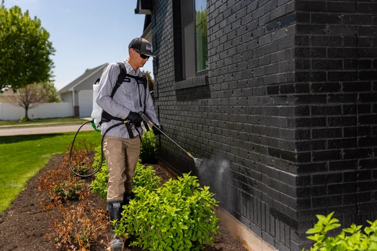 Pest control technician treating the foundation of a brick home to stop invasive bugs from entering