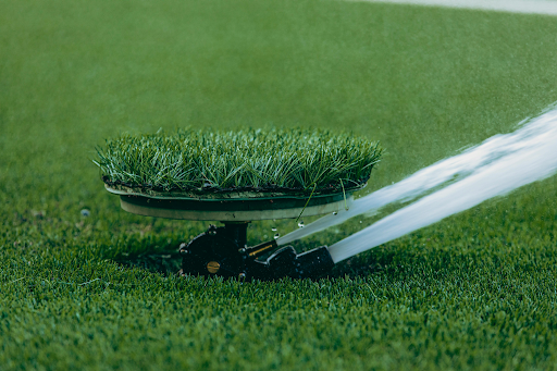 Pop-up sprinkler spraying water across a green lawn with a grass-camouflaged top cover.