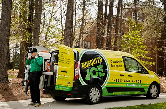 Mosquito Joe technician in green uniform loading equipment into a branded yellow and green van.
