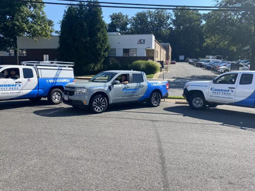 Three Connor's Pest Pros-branded vehicles are parked together in a lot with technicians inside.