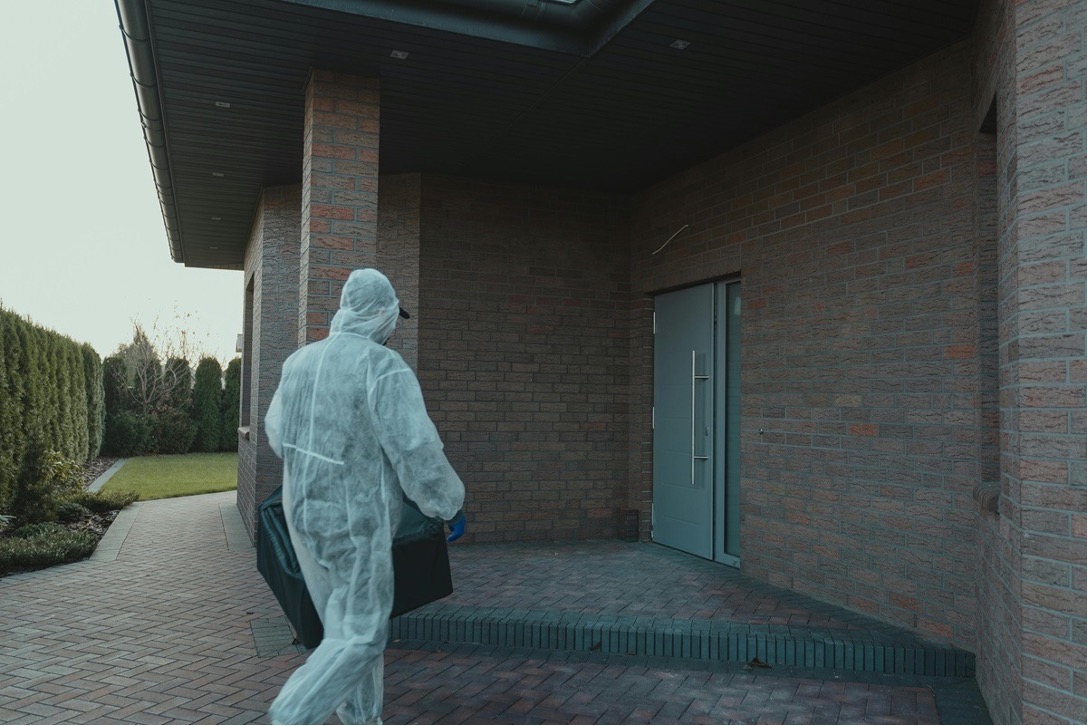Pest control technician in a protective suit conducting exterior inspection for silverfish and pest treatment