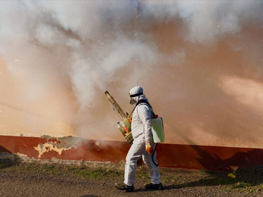 Worker in white protective suit using a fogging machine.