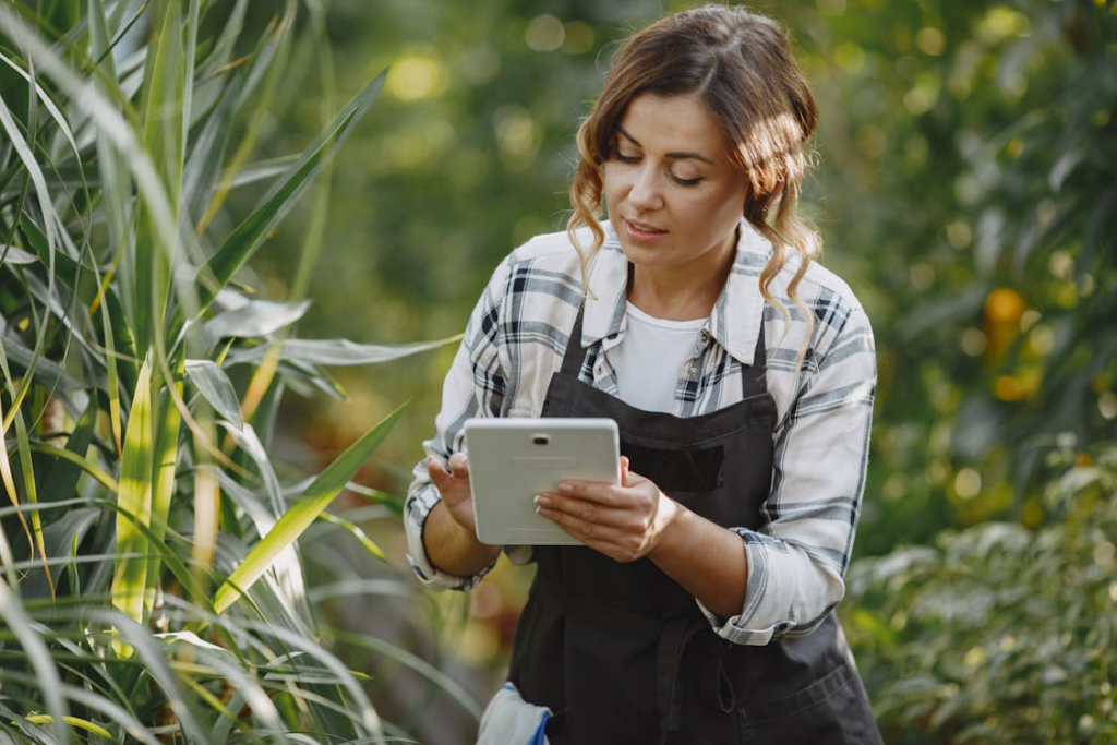 A woman wearing a black apron uses a tablet outdoors. 