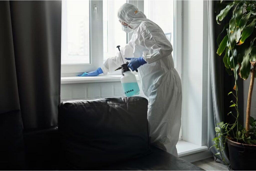 An ant exterminator in protective gear treating a residential interior with a pump sprayer. 