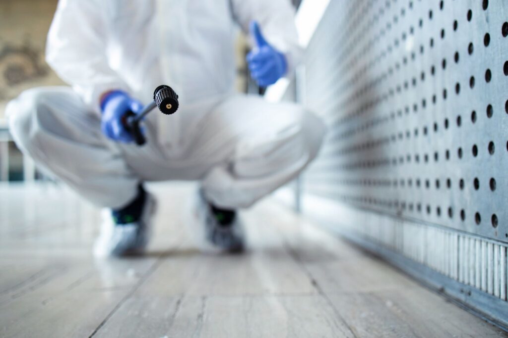 Close-up of a technician in a protective suit crouching with a spray nozzle, giving a thumbs up.