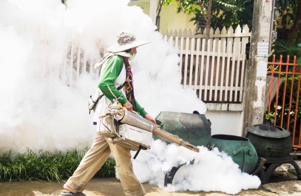 Pest control worker fogging a residential street with insecticide to kill mosquitoes.