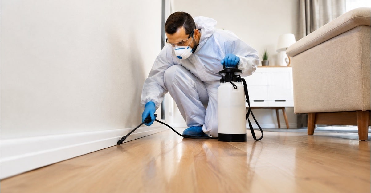 Pest control technician in protective gear spraying along the baseboard inside a Walkertown, NC home