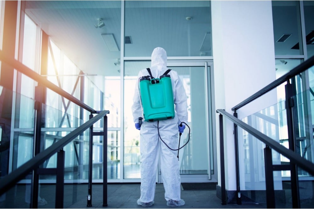 Pest control technician in a white protective suit carrying a backpack sprayer